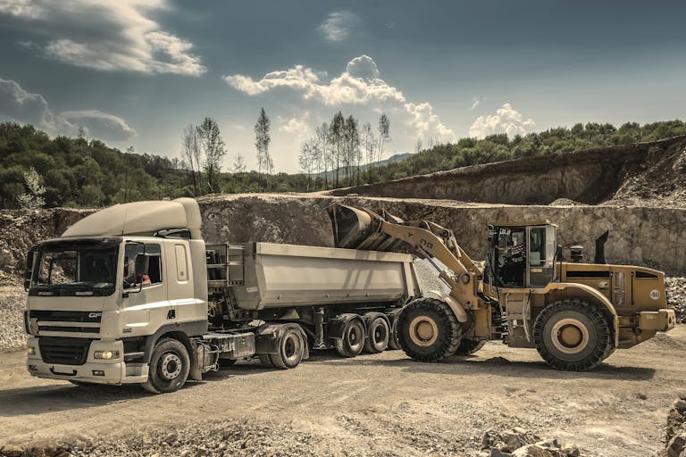 Excavator and truck working together in a quarry, showcasing industrial equipment and operations.